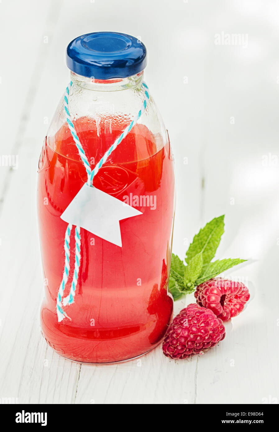 Homemade fresh raspberry juice in a glass bottle made from freshly squeezed fruit together with two fresh berries on a rustic white wooden background Stock Photo