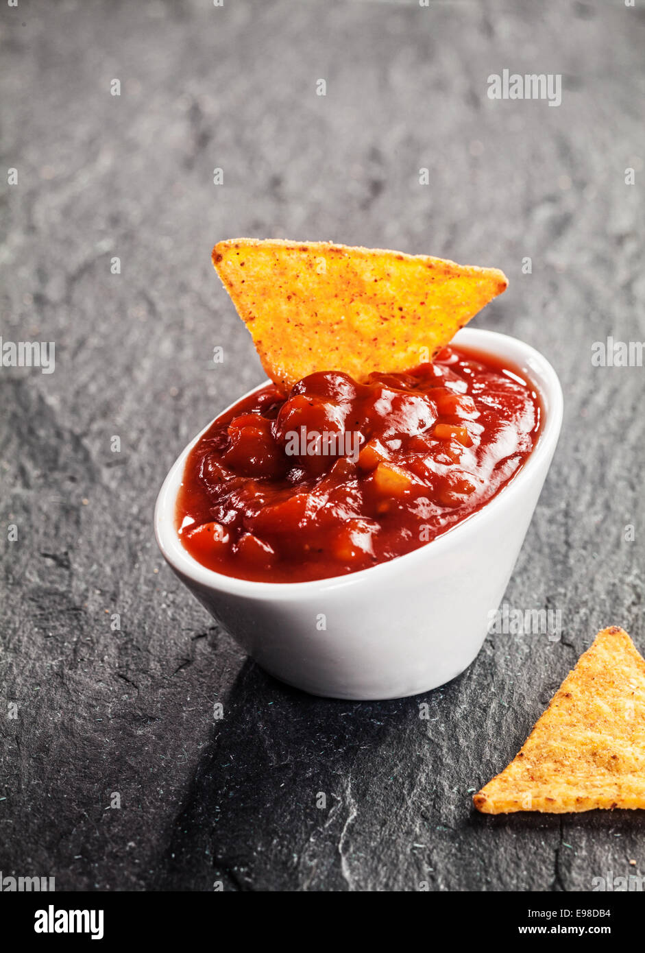 Spicy hot tomato and chili salsa dip in a small white ceramic bowl with a corn totilla for a tasty savory appetizer or snack Stock Photo