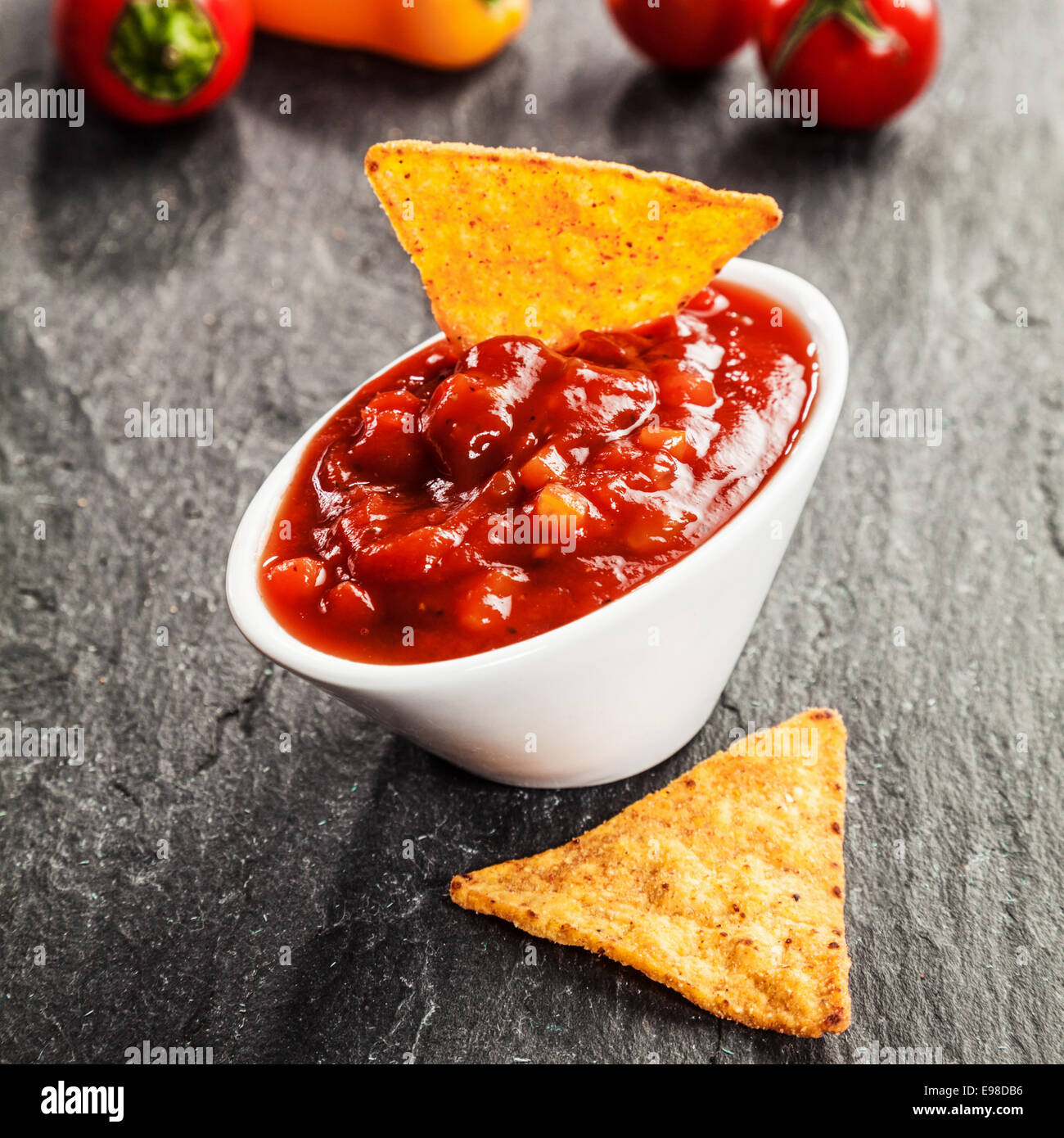 Bowl of delicious hot spicy tomato and chili salsa sauce served with triangular corn tortillas on a slate surface as a snack and appetizer Stock Photo