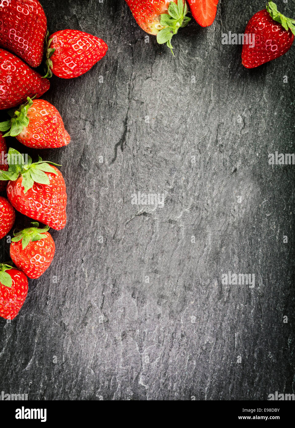 Border of whole fresh ripe red strawberries arranged on two sides on a dark grey textured slate background with copyspace and vignetting Stock Photo