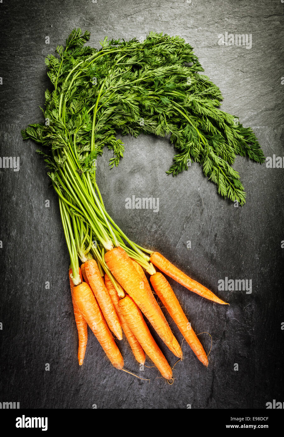 Bunch of fresh farm carrots with their green leaves at a farmers market lying on an old textured slate surface, overhead view Stock Photo
