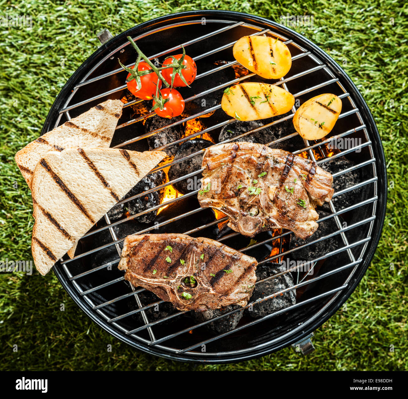 View from above of lamb chops and fresh vegetables grilling on a portable BBQ standing on grass at a summer picnic Stock Photo