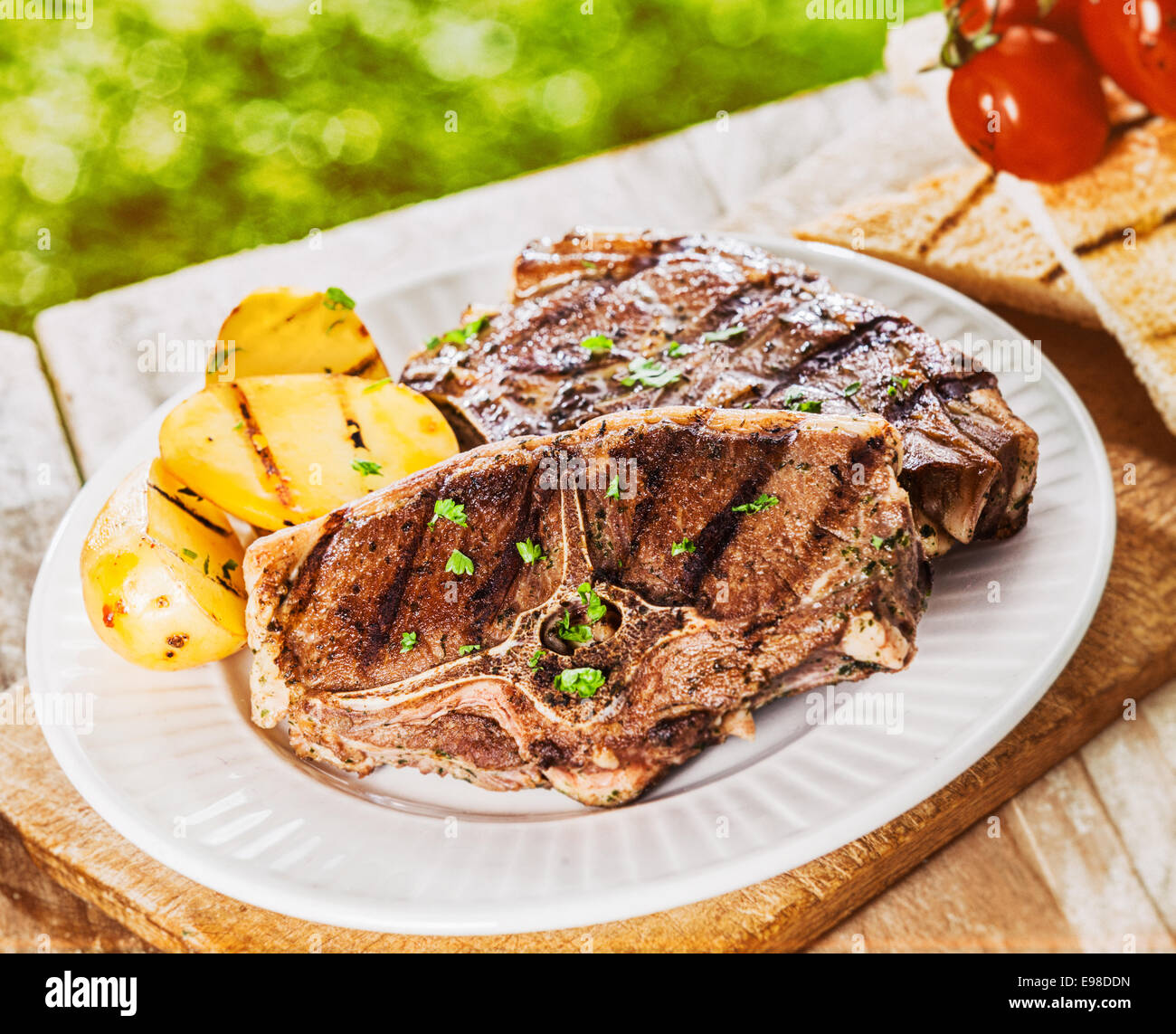 Healthy lean lamb chops with grilled potato served at an outdoor summer BBQ on a rustic wooden picnic table for a wholesome nutritious lunch Stock Photo