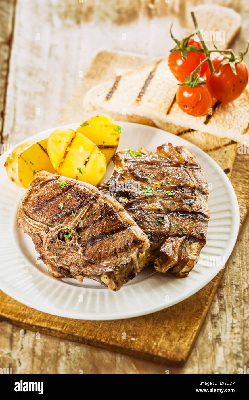 Delicious barbecued lunch on a summer picnic with grilled lamb chops, potatoes, tomatoes and slices of toast for a nutritious meal Stock Photo