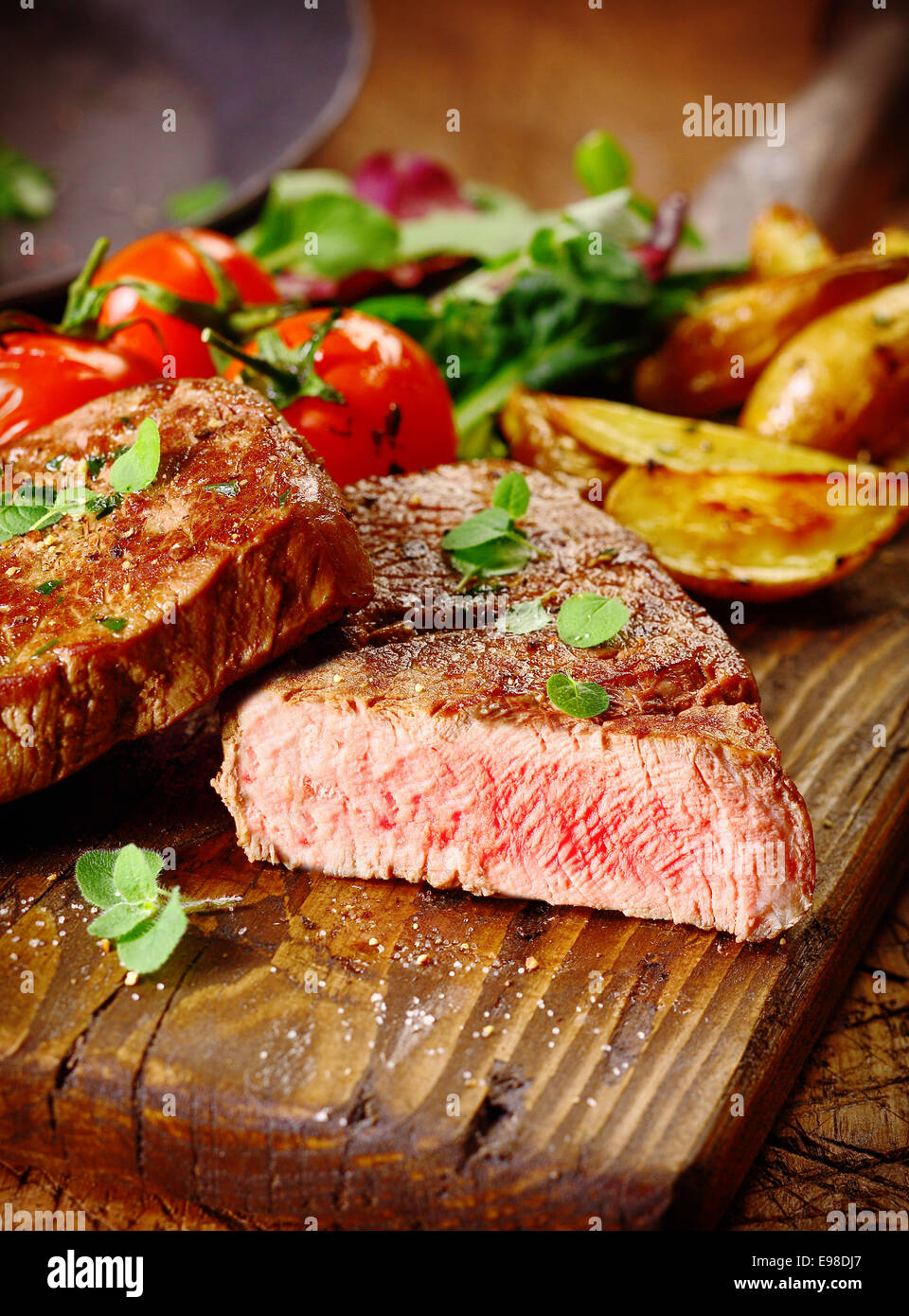 Portion of healthy lean grilled beef steak sliced through to reveal the rare interior served on a wooden board with roast vegetables Stock Photo