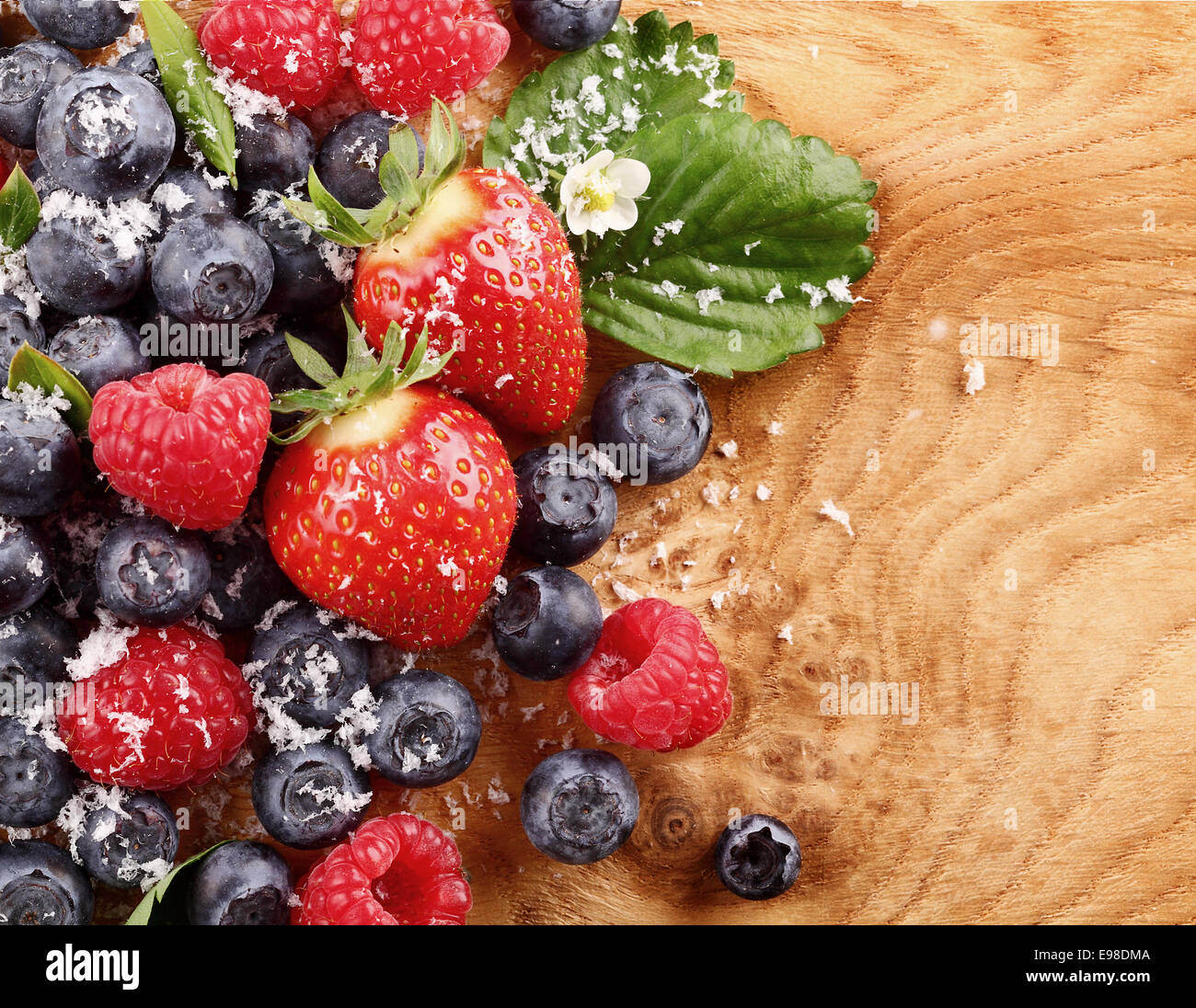 Top-view of an assortment of berries like blueberries, raspberries and strawberries over a wood table with copy-space Stock Photo