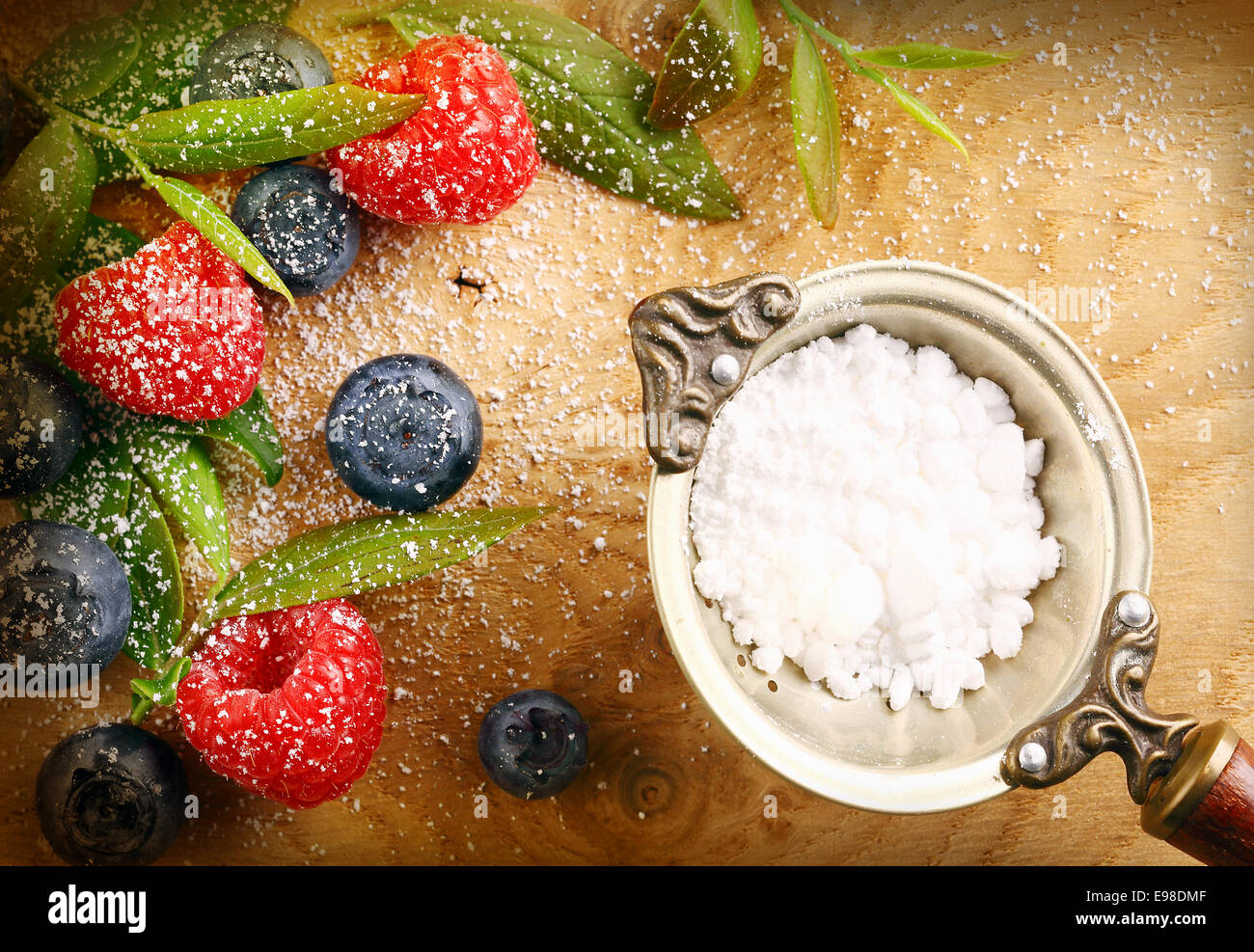 Fresh selection of mixed berries with granulated sugar in a strainer including raspberries and blueberries sprinkled with fine sugar on a wooden background Stock Photo