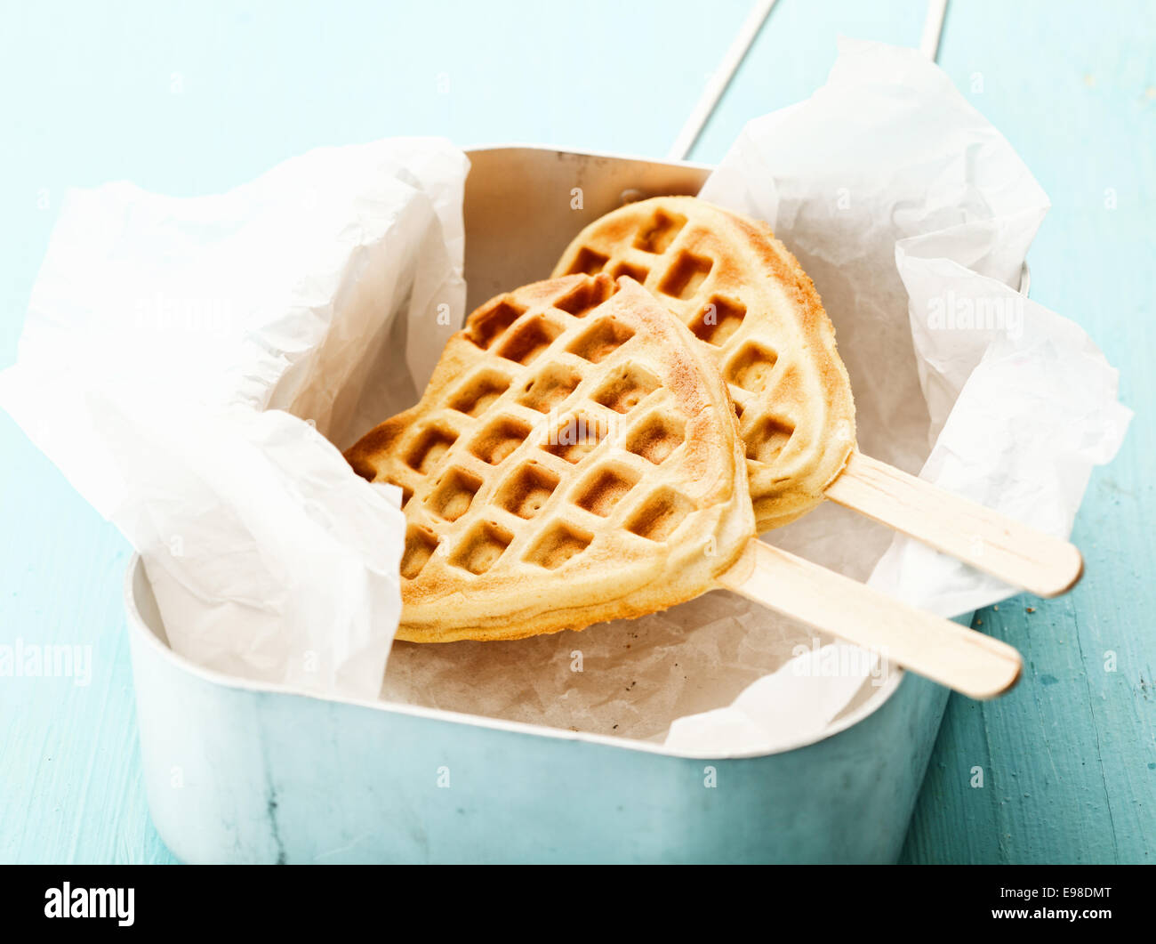 Fun crisp golden heart-shaped waffle popsicle with the traditional honeycomb pattern and a wooden stick on crumpled paper in a tin Stock Photo