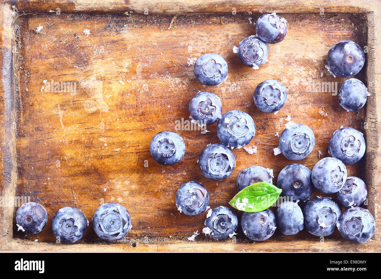 Close-up of a small amount of ripe blueberries or bilberries in an old wooden tray with a green leaf Stock Photo