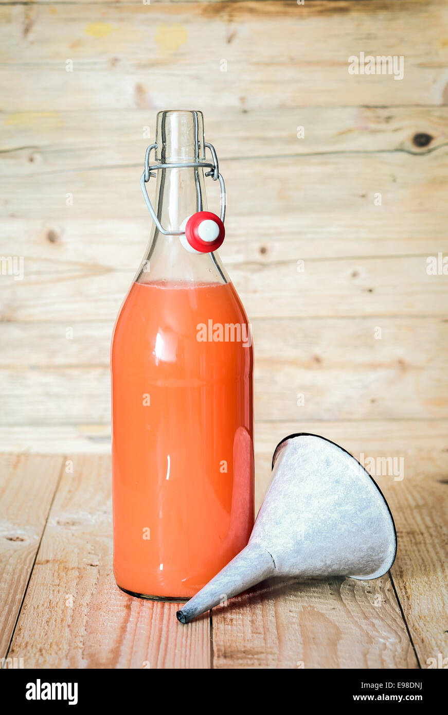 Healthy homemade mixed fruit juice blend made from a variety of liquidised fresh tropical fruit in a glass bottle with a small metal funnel in a rustic kitchen Stock Photo