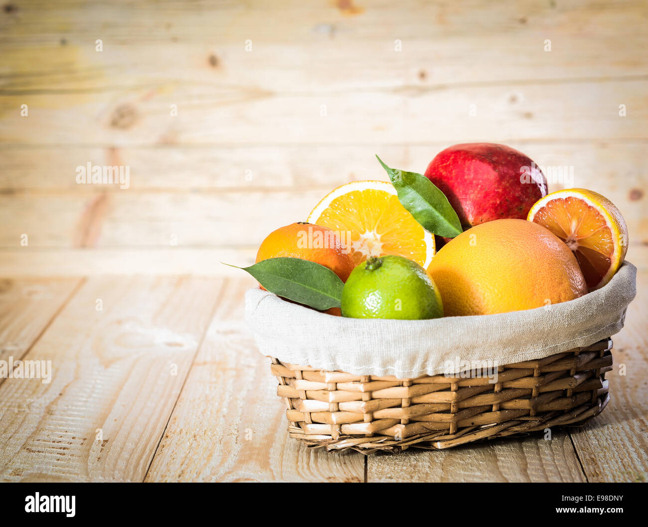Colourful wicker basket of assorted tropical fruit with a lime, grapefruit, oranges and an apple in a country kitchen on wooden Stock Photo