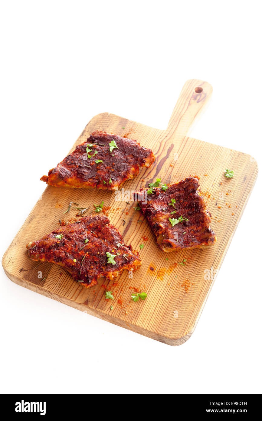 Portions of spicy BBQ ribs seasoned with aromatic condiments and fresh herbs on a wooden chopping board isolated on white Stock Photo