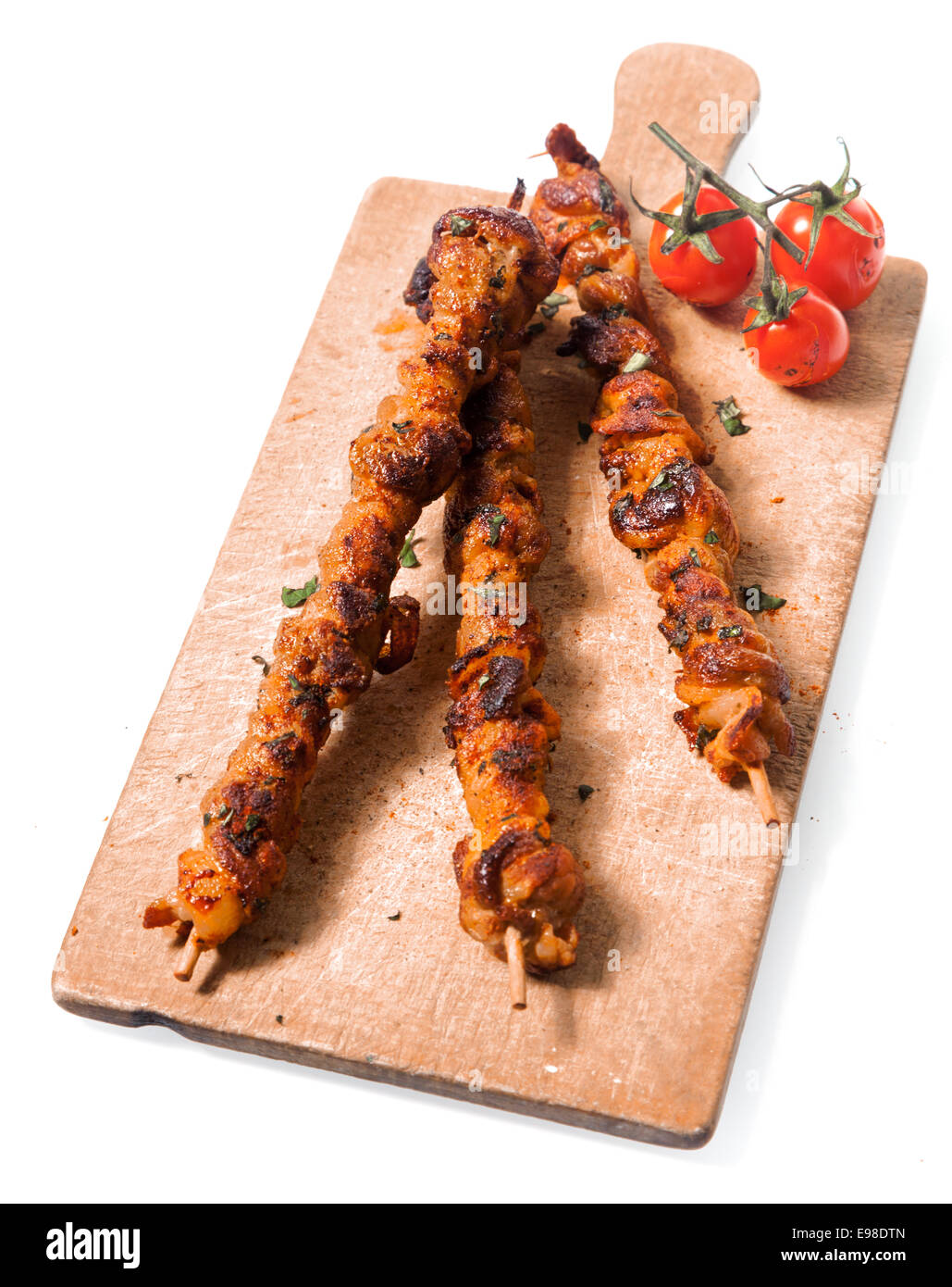 Trio of nutritious spicy grilled meat kebabs served on an old wooden board with roast cherry tomatoes, isolated on white Stock Photo