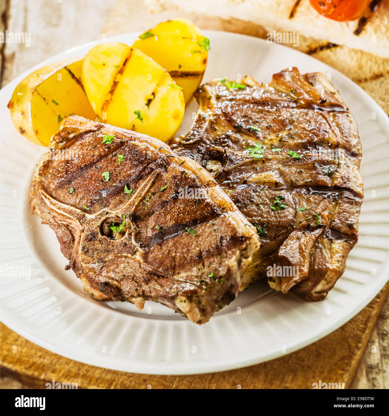 Close up of a serving of two succulent grilled barbecued lamb chops seasoned with fresh herbs served with potatoes at a summer picnic Stock Photo