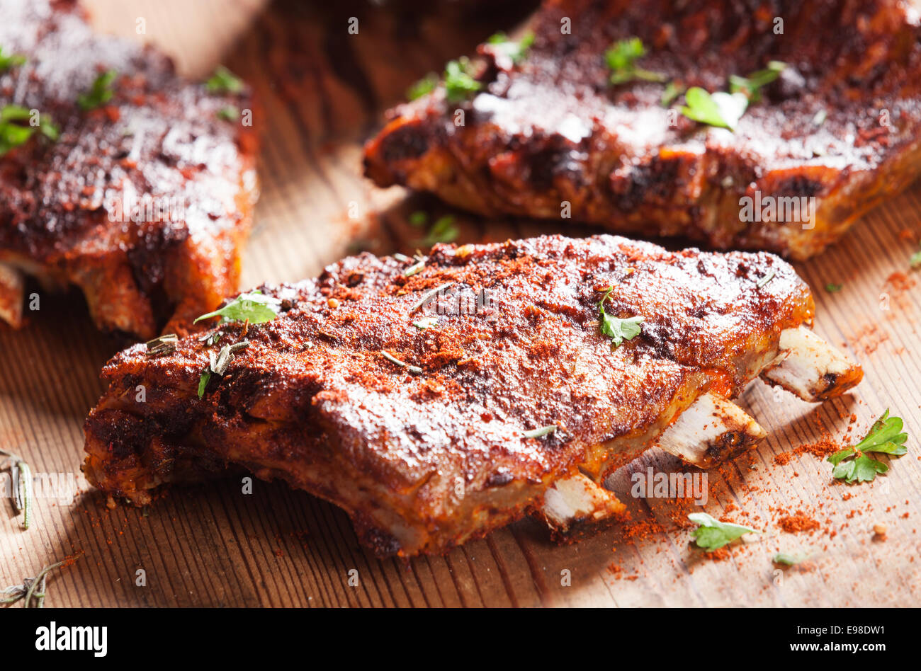 Close up of a portion of barbecued grilled ribs seasoned with hot spices and fresh herbs on a wooden board Stock Photo