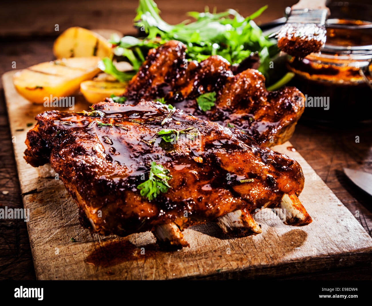 Delicious barbecued ribs seasoned with a spicy basting sauce and served with chopped fresh herbs on an old rustic wooden chopping board in a country kitchen Stock Photo