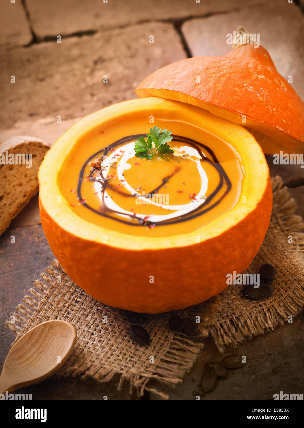 Delicious pumpkin or butternut soup served in the hollowed out gourd drizzled with cream and sauce for a hearty autumn meal Stock Photo