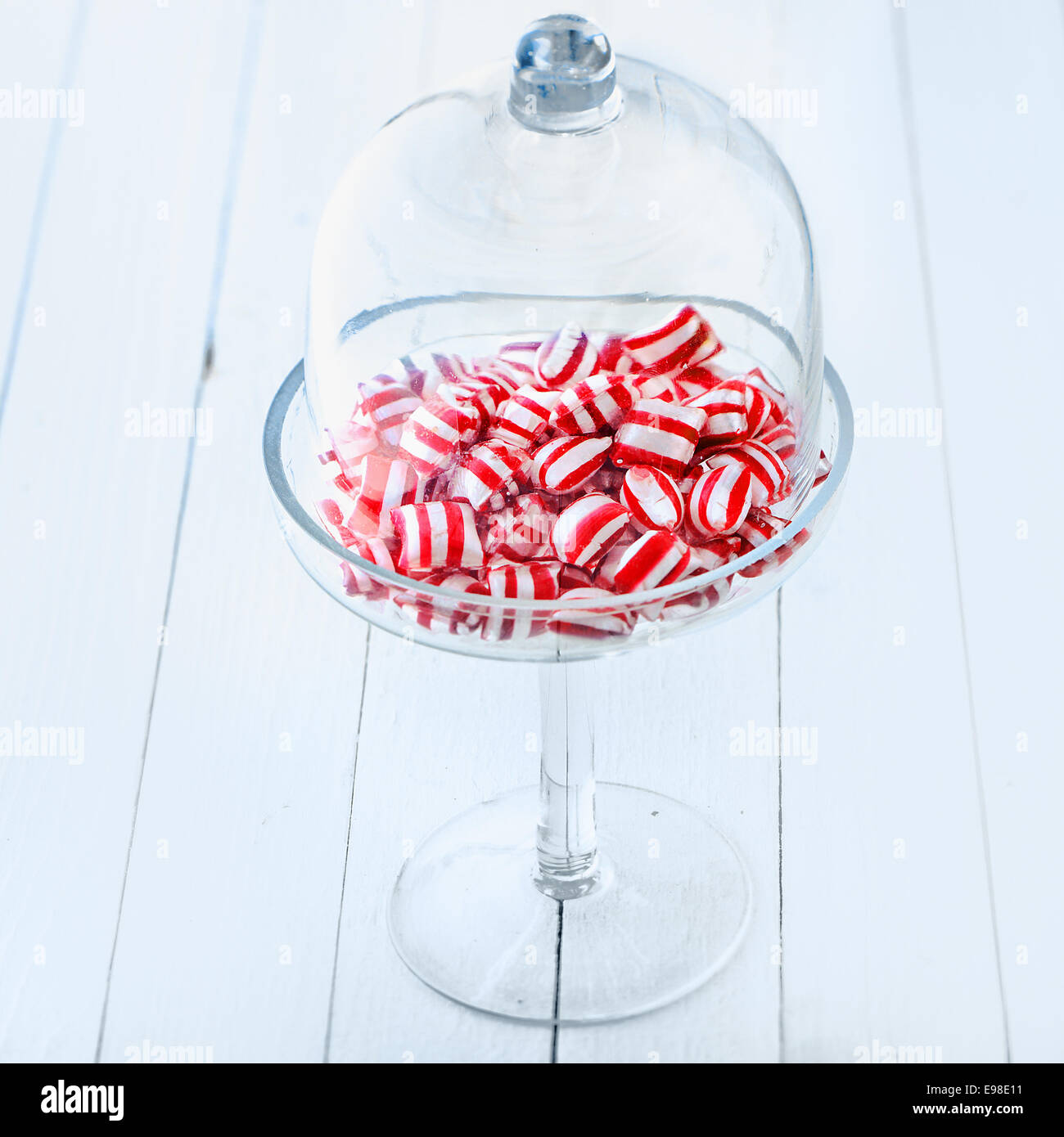 Colourful striped red and white candy in an elegant stemware glass container topped with a clear glass dome Stock Photo