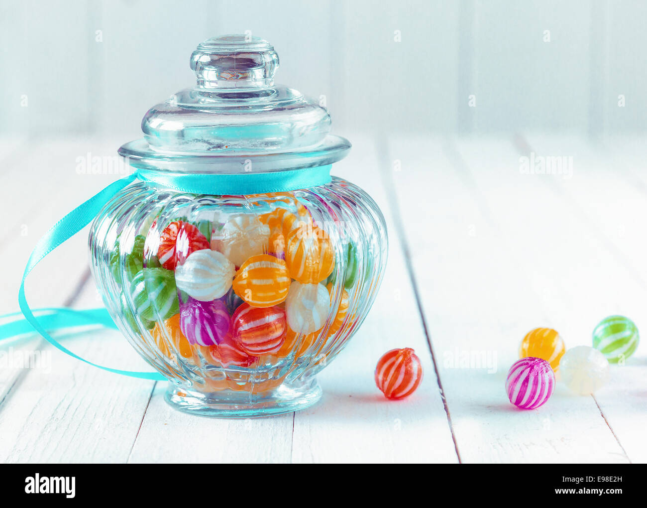 Colourful multicoloured striped candy in a decorative glass jar with a ribbed bulbous shape and a blue ribbon around the neck for a festive gift Stock Photo