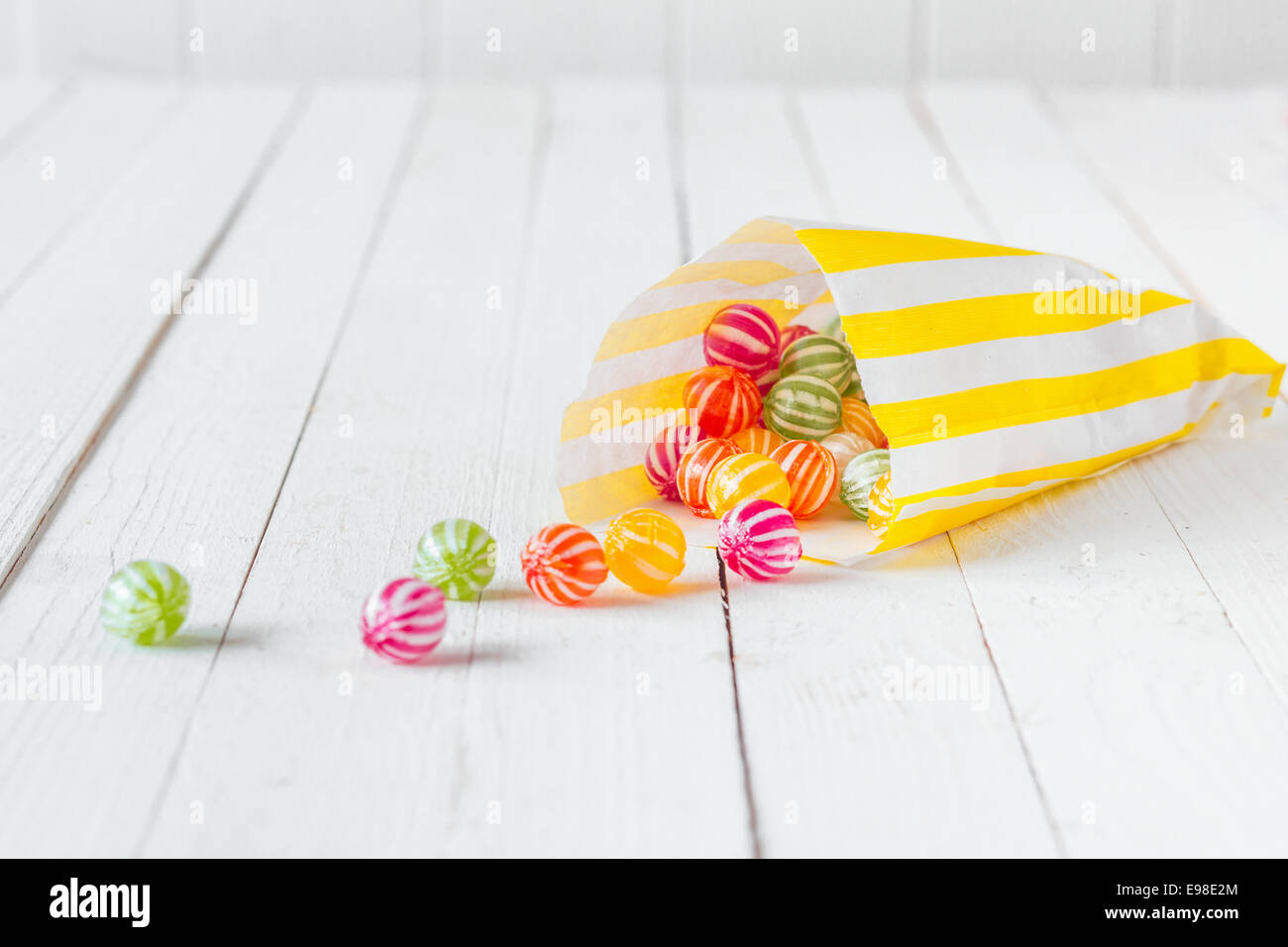 Yellow striped candy bag spilling its candies over a white wooden table Stock Photo