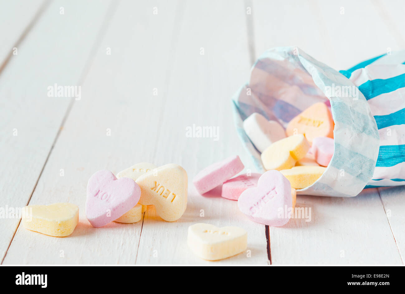 Macro of blue and white striped candy bag spilling heart shaped candies over a white wooden table Stock Photo