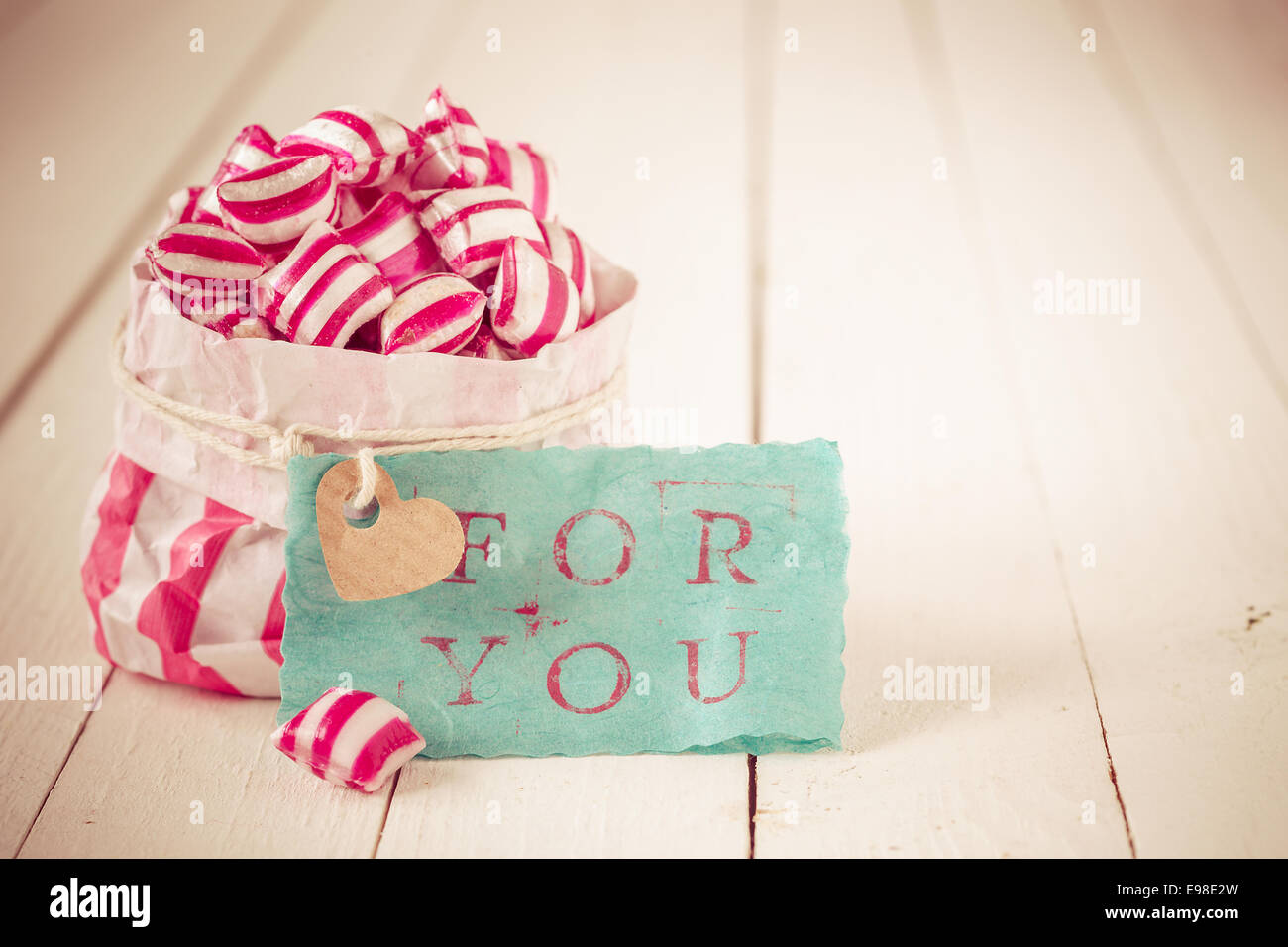 Red and white striped candy in a matching striped paper packet with a blue gift label with the words For You on a background of Stock Photo