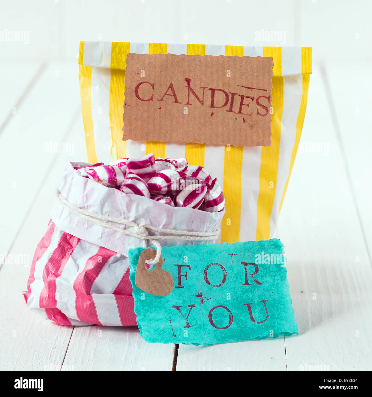Close-up of two colorful bags with white, yellow and pink stripes filled with candies with romantic message in tags meaning, Candies For You, over a white wooden background Stock Photo