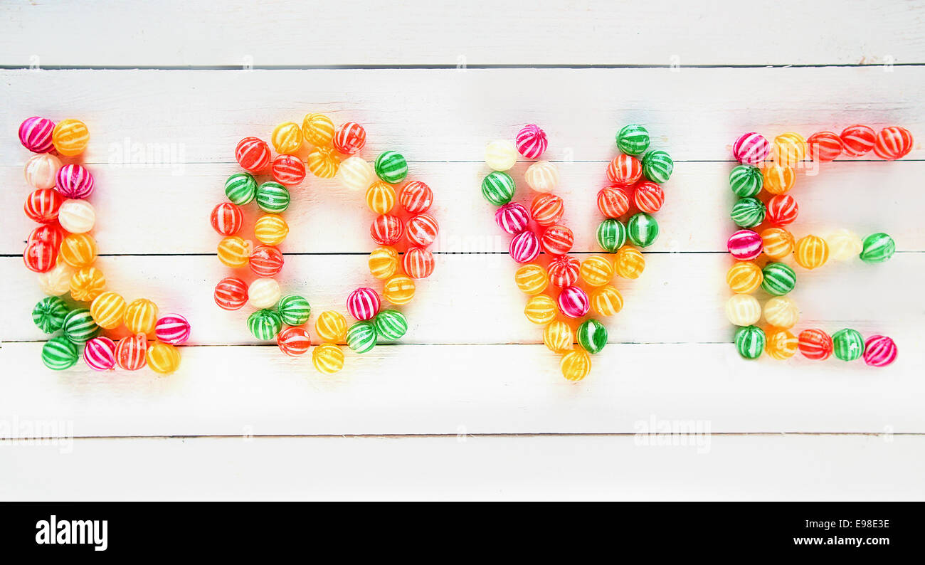 The Love word written with several types of sweet candies over a white wooden board background Stock Photo