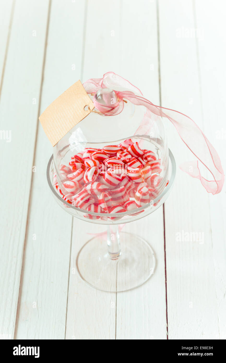 Elegant stemmed glass dish with festive striped red and white sweets and a blank gift tag Stock Photo