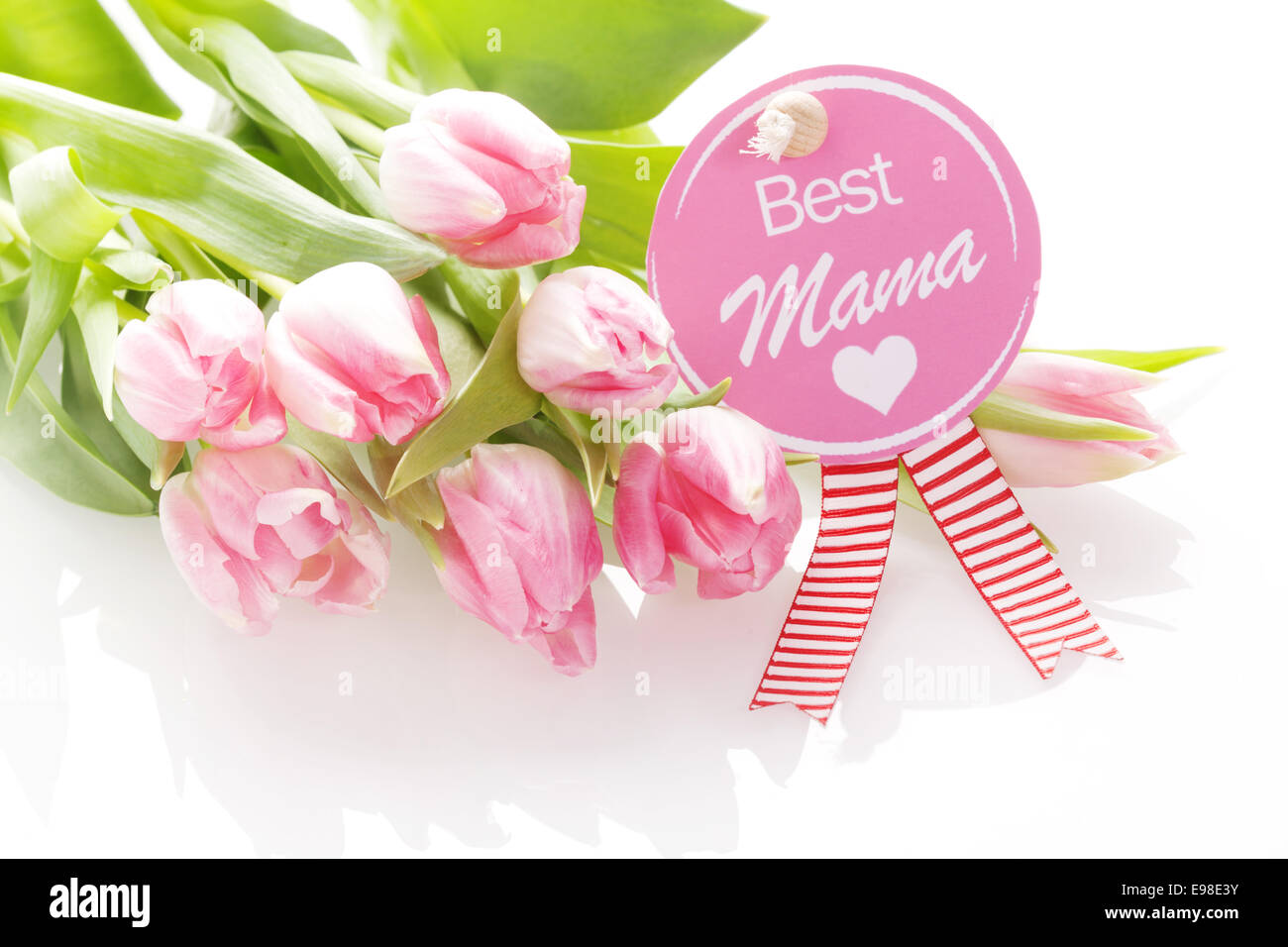 Best Mama - Mothers Day greeting on a festive circular pink rosette with the text - Best Mama - and a heart on a gift of beautiful fresh natural pink tulips Stock Photo