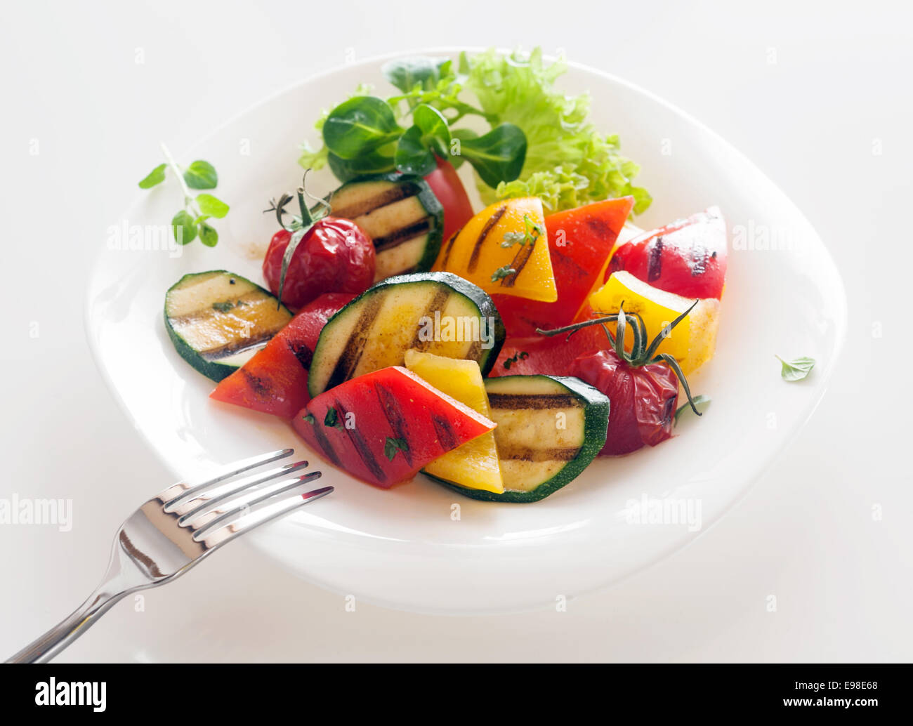 Veggie Healthy vegetarian and vegan cuisine of roasted diced fresh vegetables including baby marrow, tomato and sweet peppers garnished with herbs and frilly green lettuce Stock Photo