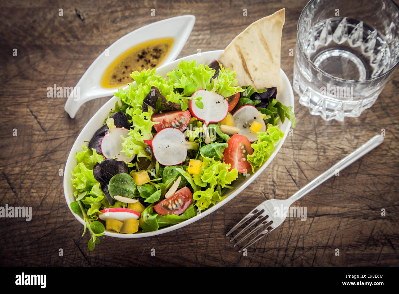 Healthy leafy green mixed salad with fresh spring ingredients on a grunge wood table with a savory oil salad dressing, view from above Stock Photo