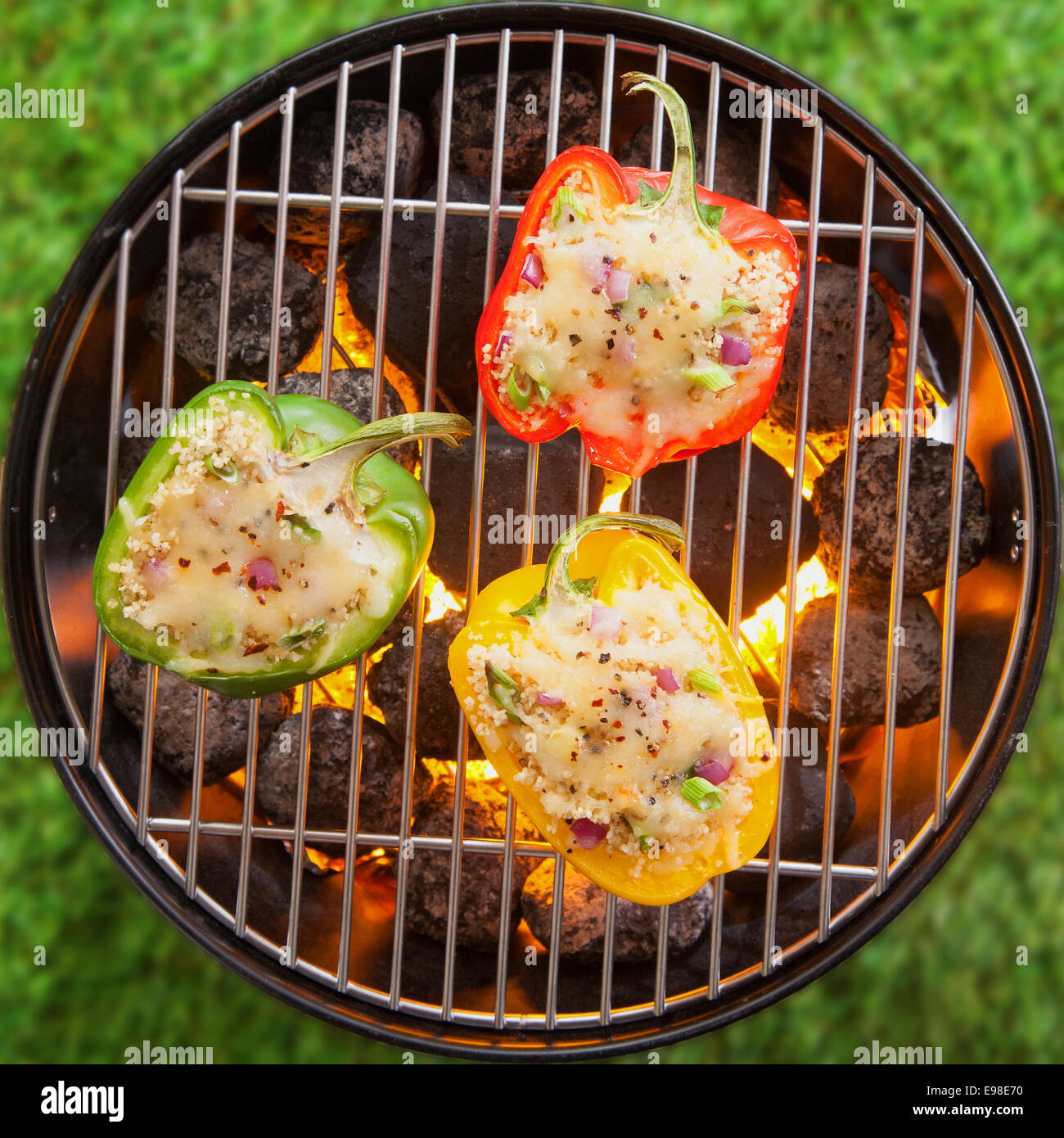 Overhead view on green grass of grilling stuffed savory bell peppers topped with melted cheese over the fire on an outdoor summer BBQ or picnic Stock Photo
