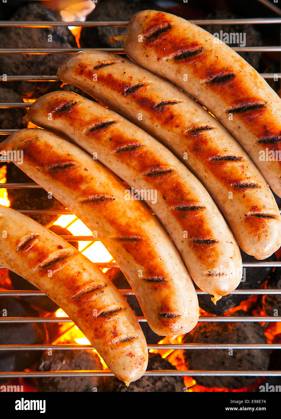 Row of tasty browned seared pork and beef sausages cooking over the hot coals on a barbecue fire, close up overhead view Stock Photo