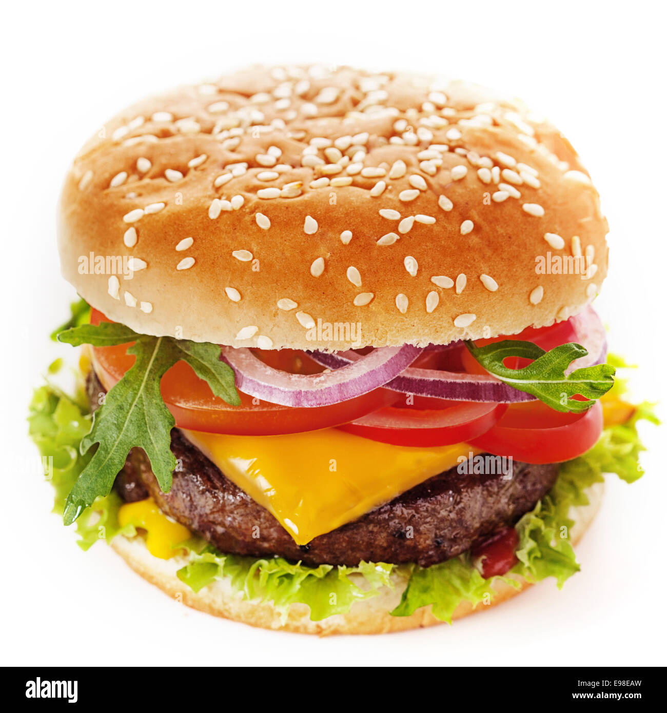 Close-up of a tasty cheeseburger made of green salad and ground meat patty topped with sliced tomato, onion, cheese, parsley and sweet ketchup, placed inside a sliced hamburger bun with sesame Stock Photo