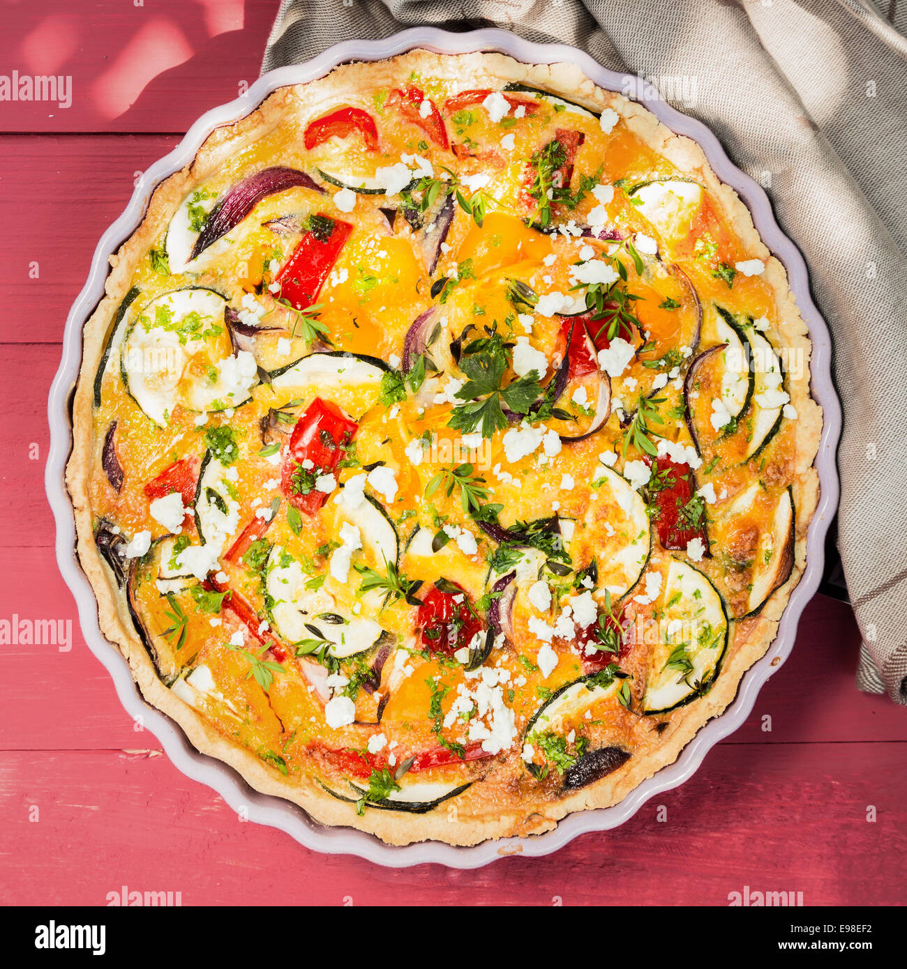 Delicious savory tart or quiche with brinjals or eggplant, pepper, tomato and cheese sprinkled with fresh chopped herbs, overhead view Stock Photo