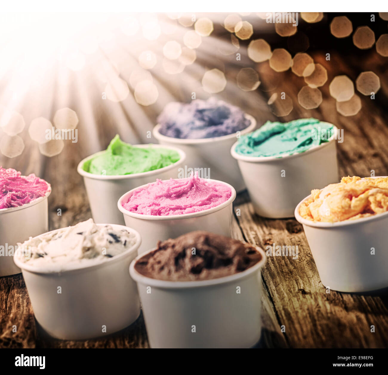 Selection of colorful tubs of frozen multicolored ice cream standing on a rustic wooden table on a hot summer day with a sunbusrt and flare effect Stock Photo