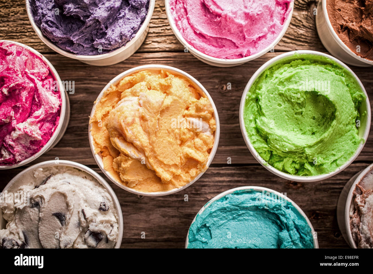 Array of different flavored colorful ice cream in plastic tubs displayed on an old wooden table at an ice cream parlor for delicious frozen snacks on a hot summer day Stock Photo