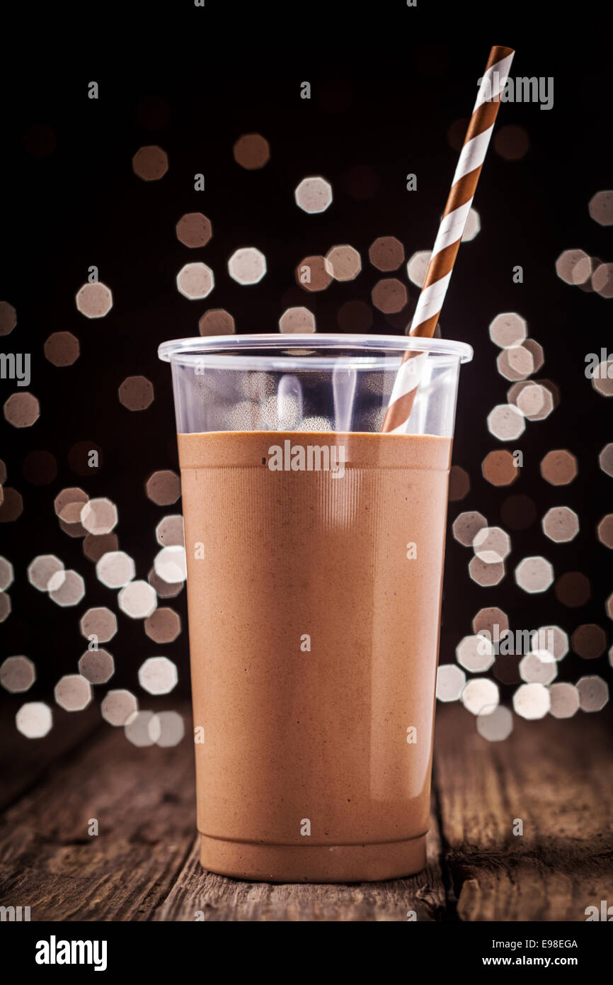 Plastic glass of delicious creamy chocolate smoothie or milkshake against a background of sparkling festive party lights Stock Photo