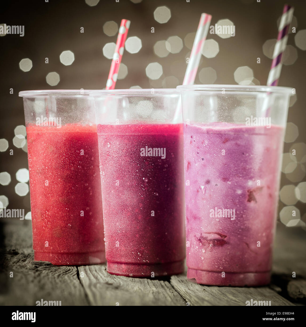 Trio of healthy assorted berry smoothies including strawberry and blueberry blended with yogurt or ice cream standing in a row against a bokeh of party lights Stock Photo