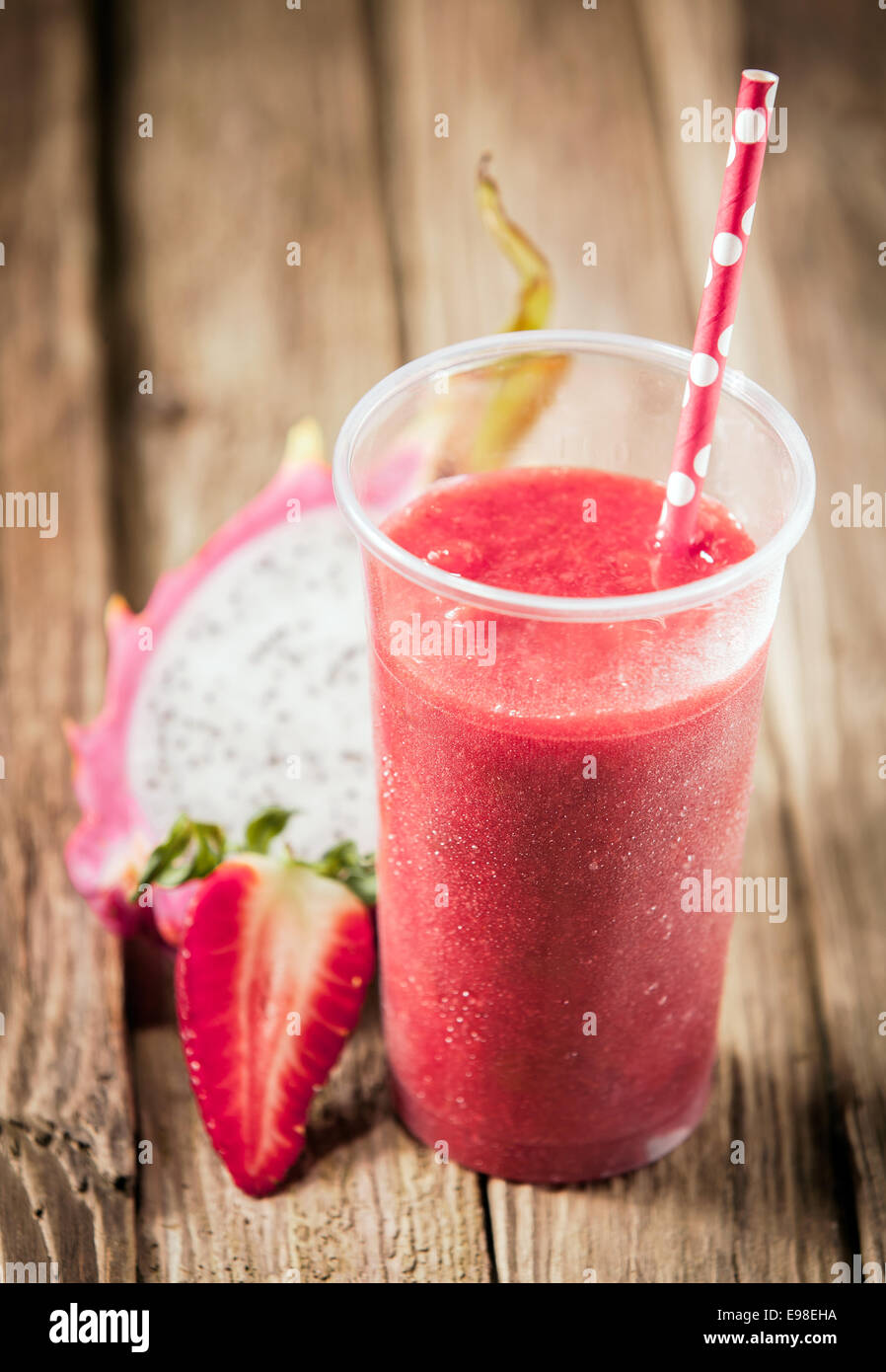 Healthy nutritious tropical smoothie with strawberries and dragon fruit blended with yoghurt or ice cream on a rustic wooden table top Stock Photo