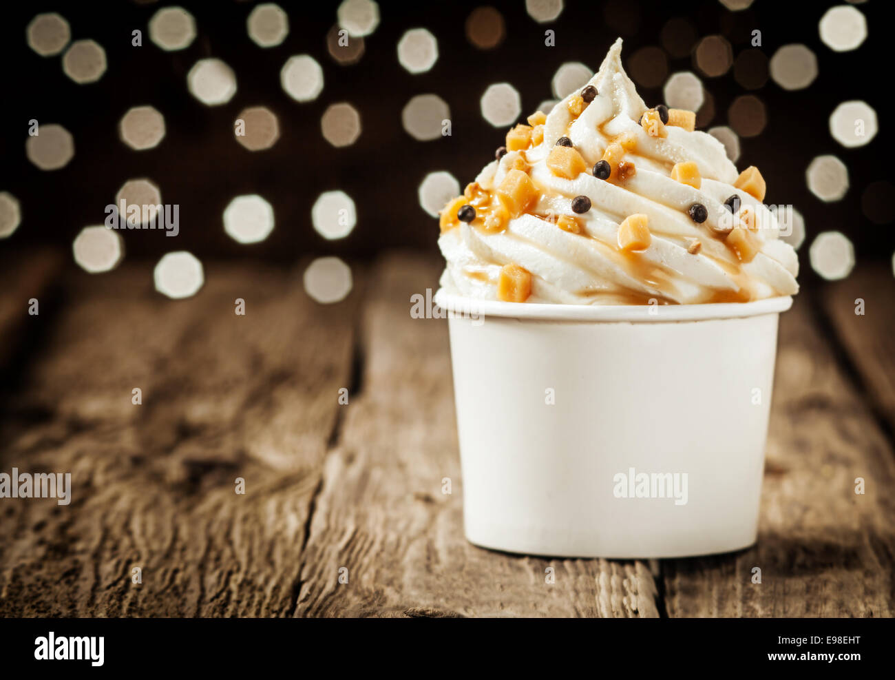 Delicious frozen yogurt party dessert twirled in a tub and decorated with sprinkles against a sparkling bokeh of festive lights Stock Photo