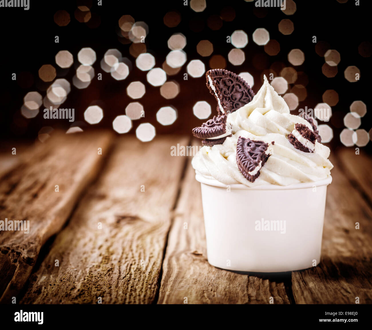 Delicious party dessert with frozen yogurt and chocolate oreos in a plastic takeaway tub standing on an old wooden counter with Stock Photo