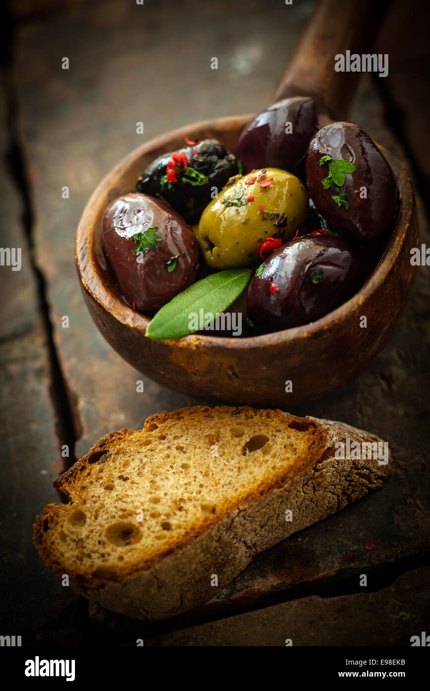 Spicy olive appetizer with preserved black and green olives topped with hot chilli seasoning in an old wooden ladle served with Stock Photo