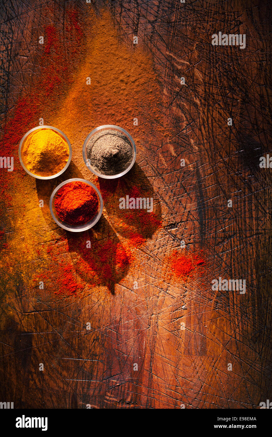 Cooking using fresh ground spices with three small bowls of spice on a wooden table with powder spillage on its surface, overhead view with copyspace Stock Photo