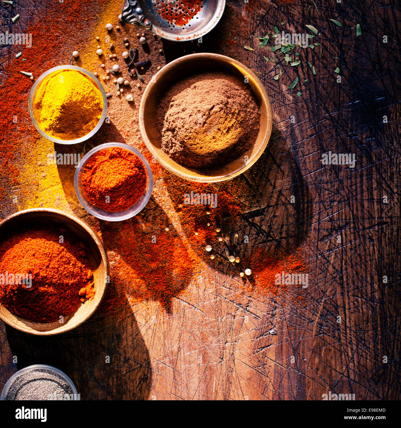 Overhead view depicting cooking with spices in a rustic kitchen with bowls of colourful ground spice and scattered powder on an Stock Photo
