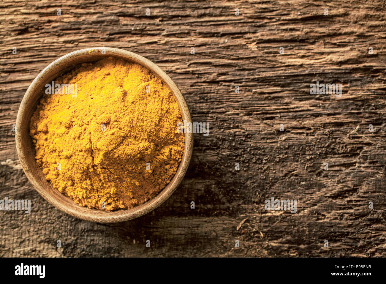 Asian curry powder made from a blend of spices with a masala or turmeric base in a small bowl on a grunge textured wooden surface, overhead view with copyspace Stock Photo