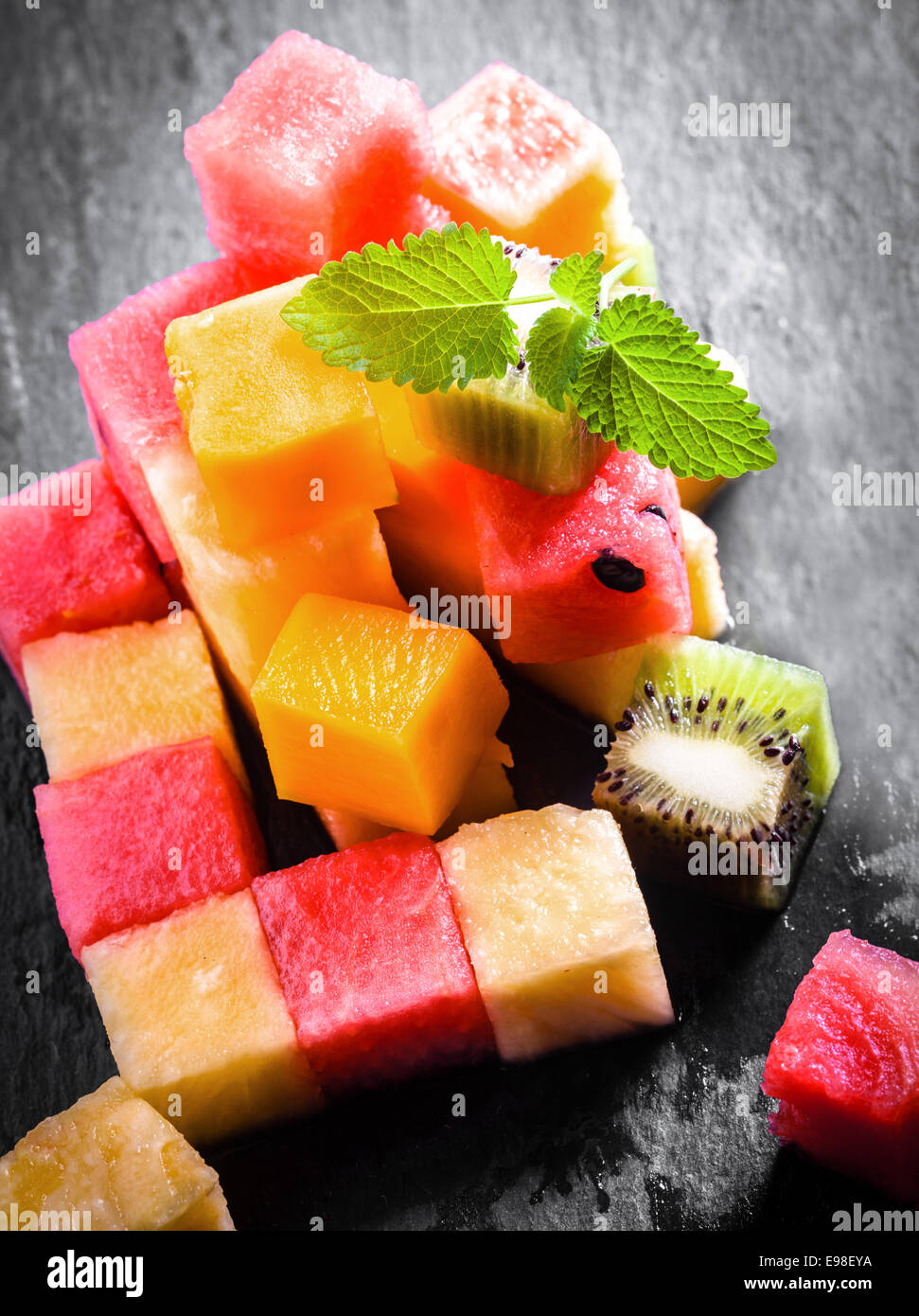 Pile of diced and cubed fresh summer fruit being prepared for a gourmet dessert with watermelon, pineapple, melon, orange, and kiwifruit on a slate kitchen counter Stock Photo