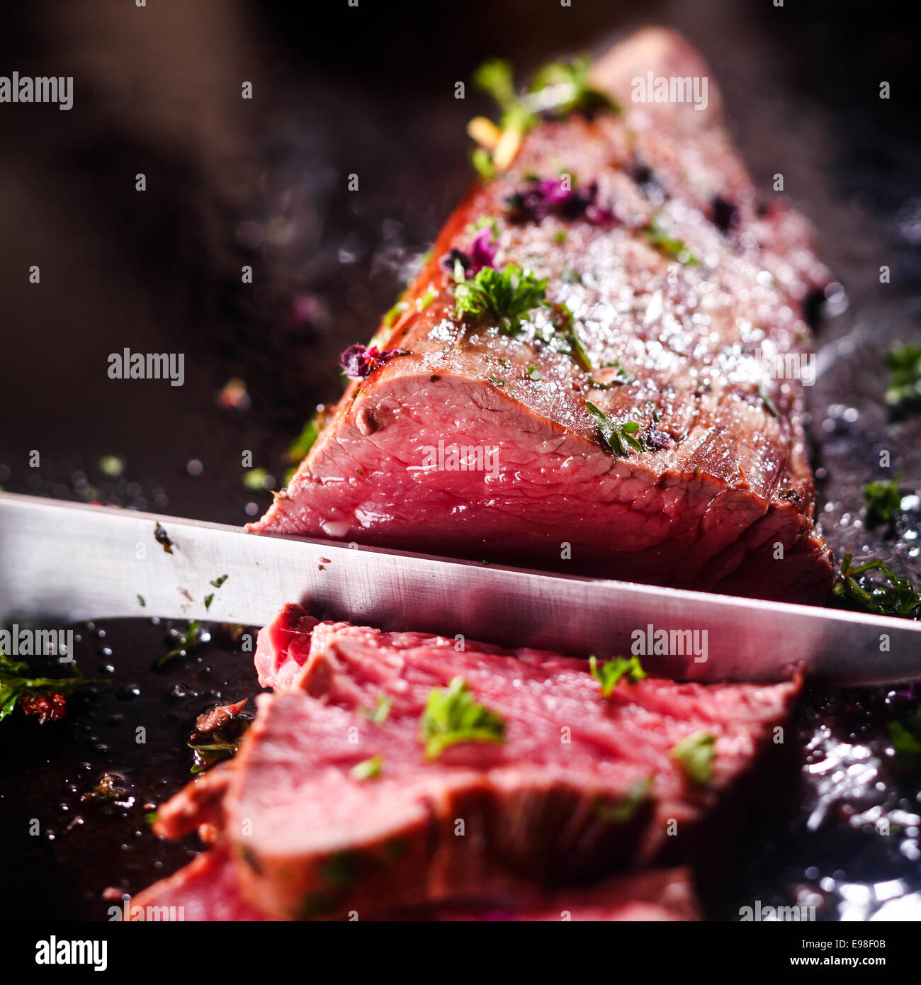 Carving a portion of delicious rare roast beef sirloin of fillet seasoned with fresh herbs with a large steel carving knife Stock Photo