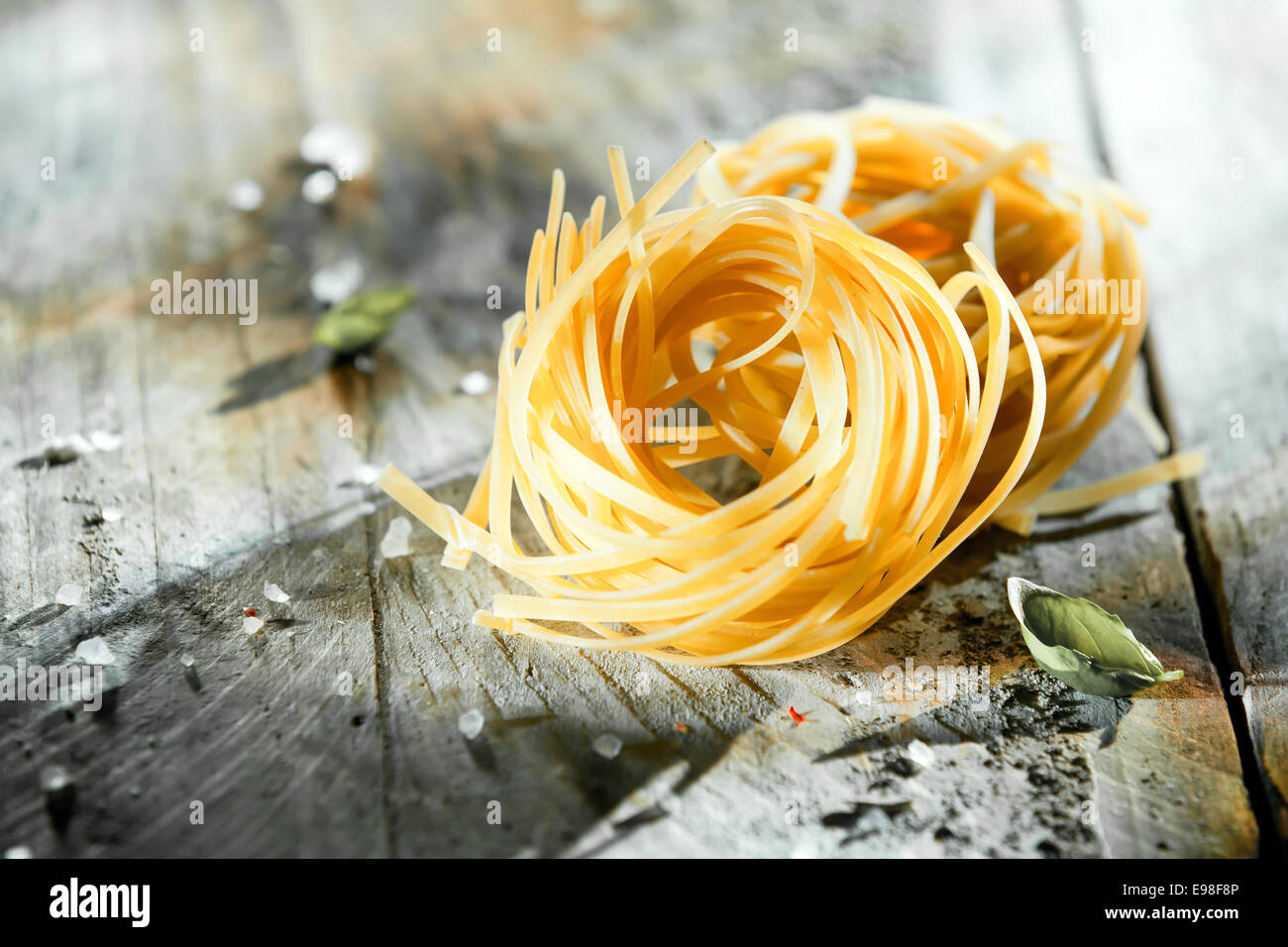 Dried Italian linguine or tagliatelli pasta in coils lying on a rustic grungy grey wooden background with copyspace Stock Photo
